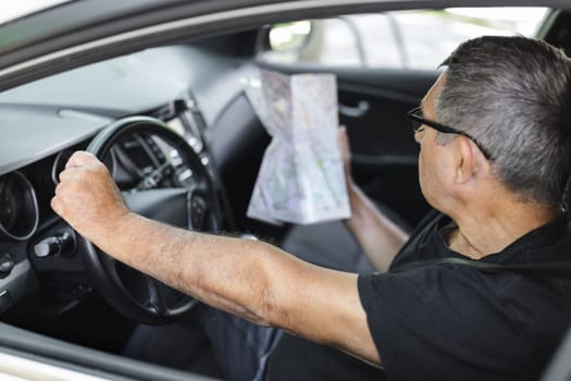 Senior behind the steering wheel of a car, looking at map for directions