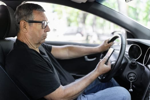 Active senior in his 70s driving a car and usig his mobile phone