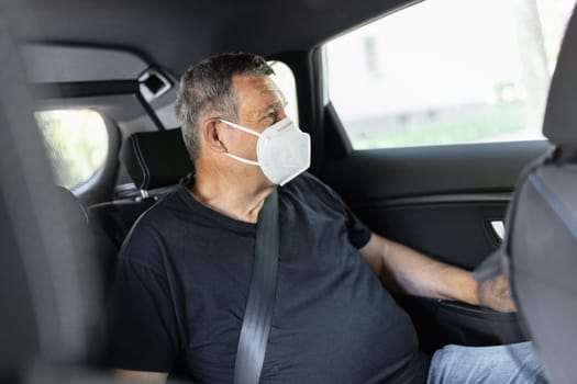 Senior in his 70s sitting at the back of car wearing a face mask for protection against corona virus