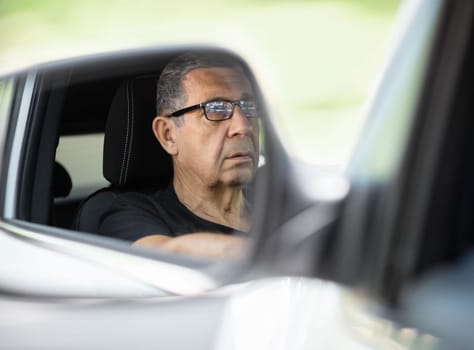 Happy senior in his 70s driving a car