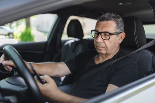 Active senior in his 70s driving a car and usig his mobile phone