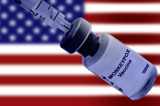 Monkeypox vaccine with a syringe close-up against the background of a blurred US national flag.