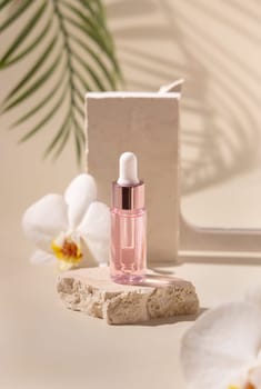 Dropper Bottle on stone near white orchid flowers and palm leaves on light yellow, close up, mockup. Skincare beauty product, essential oil or serum. Exotic cosmetics, pastel minimal composition..