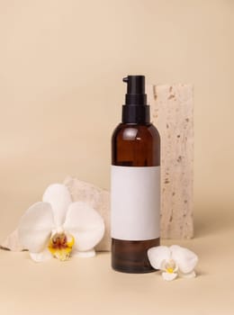 Dark glass cosmetic bottle with blank label near white orchid flowers and stones on light yellow, close up, mockup. Skincare handmade beauty product, tonic or lotion. Exotic natural cosmetics..