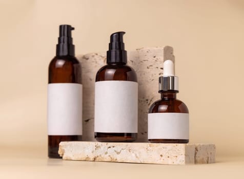 Brown glass one pump bottles on travertine stones on light beige close up, label mockup. Skincare beauty product package. Natural cosmetics, minimal composition..