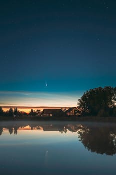 Dobrush, Belarus. Comet Neowise C2020f3 In Night Starry Sky Reflected In Small Lake Waters