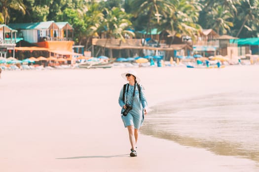 Canacona, Goa, India. Young Caucasian Lady Woman With Camera Walking Along Seashore On Palolem Beach In Summer Sunny Day.