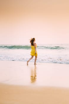 Goa, India. Young Caucasian Woman In Yellow Dress Enjoying Life And Running Towards Sea Waves