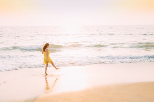 Goa, India. Young Caucasian Woman In Yellow Dress Walking Along Seashore In Summer Sunlight.