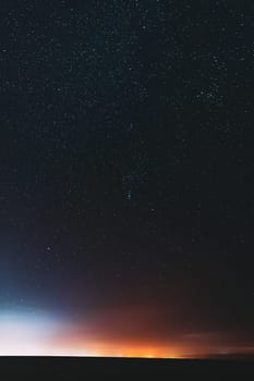 Night Starry Sky With Glowing Stars Above Countryside Landscape. Rural Field Meadow In Early Spring. Bright Glowing Stars.