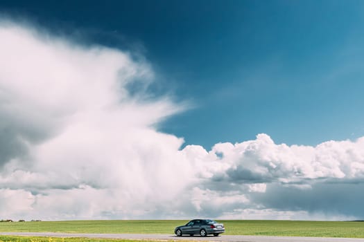 Car Moving On Country Road On Background Of Green Spring Fields Or Meadow In Sunny Day With Beautiful Blue Sky.