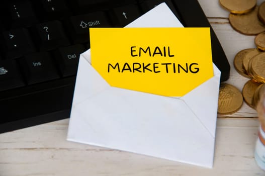 Email marketing text on yellow notepad in an envelope on keyboard computer with gold coins. Online business concept