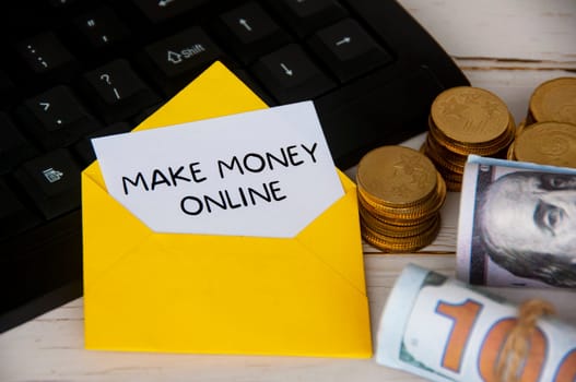Make money online text on white notepad in yellow envelope on keyboard computer with gold coins and bank notes. Online business concept