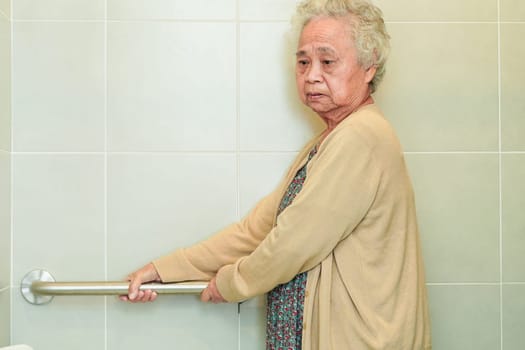 Asian elderly old woman patient use toilet support rail in bathroom, handrail safety grab bar, security in nursing hospital.