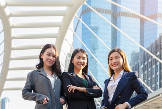 Outdoor portrait of attractive three young lady in suits standing together with city buildings on background. Successful businesswomen smiling and looking at camera.Female business team concept