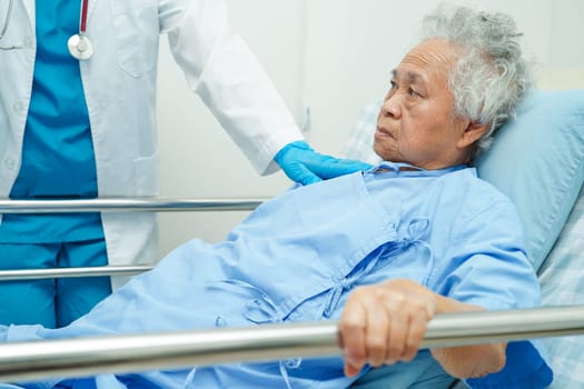 Asian elder senior woman patient holding bed rail while lie down with hope waiting her family in hospital.