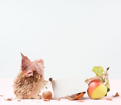 Autumn background with colorful leaves, a blank tag, a hedgehog and an apple, rose colored template and greeting card