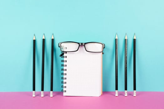 Empty notebook with a pencils and eyeglasses on a pink and blue background, brainstorming for new ideas, writing a message, home office desk