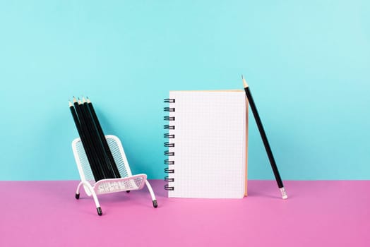 Empty notebook with pencils in a chair, being creative and brainstorming for new ideas, writing a message, workspace, pink and turquoise colored background