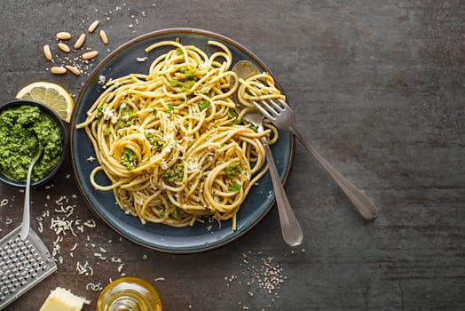 Eating hot spaghetti with fresh basil pesto and parmesan cheese. Top view of plate with spaghetti in pesto sauce with basil on dark background
