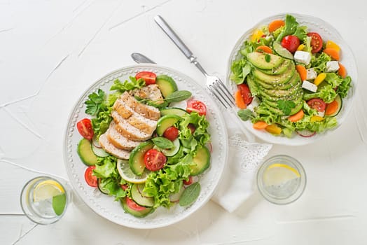 Healthy green salads with chicken, avocado, feta cheese and fresh vegetables on white background