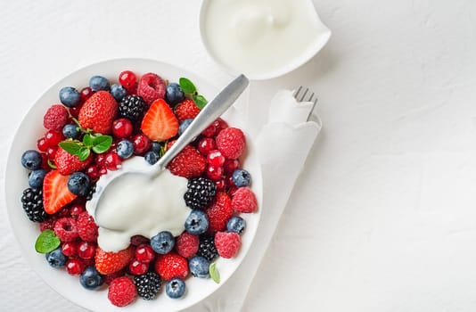 Bowl of healthy fresh berry fruit meal with cream on white background. Top view. Berries overhead closeup colorful assorted mix of strawberry, blueberry, raspberry, blackberry, red currant