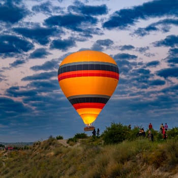 GOREME/TURKEY - June 30, 2022: hot air balloon flies over the tourists near the hills of goreme.