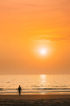 Dark Silhouette Of Young Caucasian Lady Woman In Swimsuit Walking In Sea Beach During Sunset. Vacation On Ocean Beach. Sundown Above Sea Horizon At Sunset. Natural Sunrise Sky Warm Colors Over Ocean.