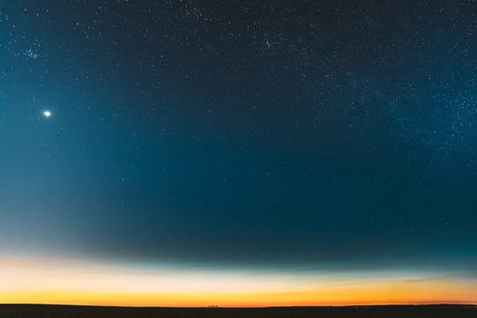Night Starry Sky With Glowing Stars Above Countryside Field Landscape In Early Spring. Bright Glow Of Planet Venus In Sky Among The Stars. Sky In Warm Lights Of Evening Sunset Dawn Or Morning Sunrise.