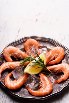 Fresh shrimps with rosemary spices and lemon on ice in silver plate. Top view of seafood ingredients with copyspace.