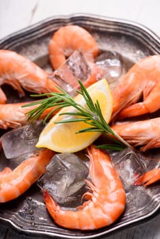 Fresh shrimps with rosemary spices and lemon on ice in silver plate. Cloeup of seafood ingredients.