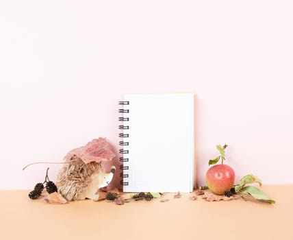 Empty notebook with an apple and a hedgehog, autumn background with colorful leaves, office desk, pastel color