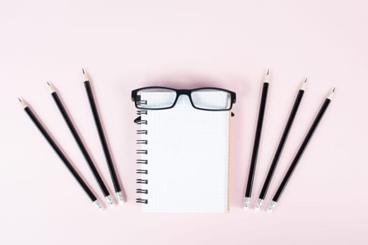 Empty notebook with pencils and eyeglasses on a rose background, brainstorming for new ideas, writing a message, home office desk