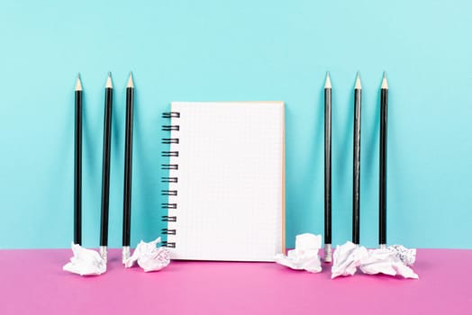 Notebook with copy space, pencils and crumpled up paper on a pink and blue background, brainstorming for new ideas, writing a message, home office desk