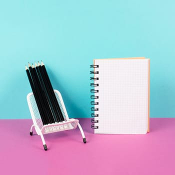 Empty notebook with pencils in a chair, being creative and brainstorming for new ideas, writing a message, workspace, pink and turquoise colored background