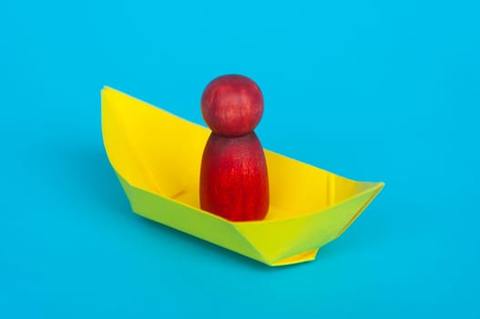 Red wooden figure on yellow paper ship with blue background. Copy space.