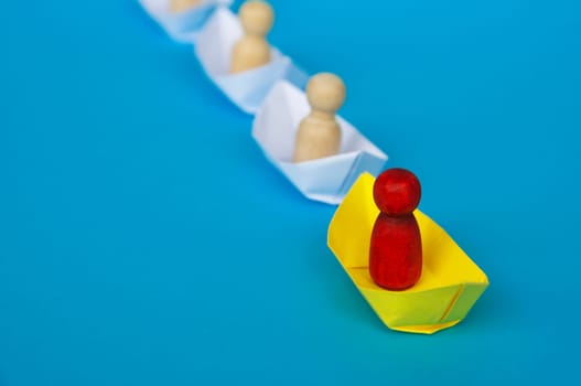 Leadership Concept - Red wooden figure on yellow paper ship origami leading the rest of the figure on white paper ship. Copy space.