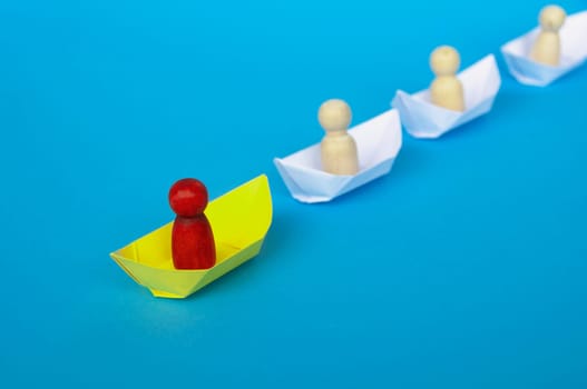 Leadership Concept - Red wooden figure on yellow paper ship origami leading the rest of the figure on white paper ship. Copy space.