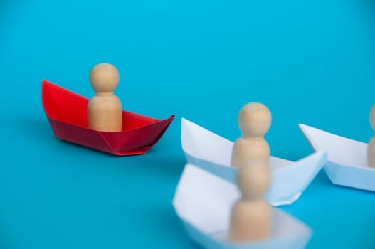 Leadership Concept - Wooden figure on red paper ship origami leading the rest of the figure on white paper ship. Copy space.
