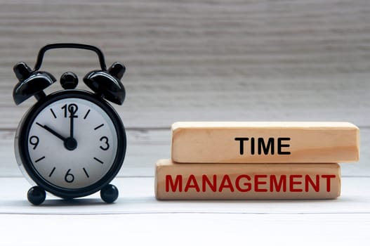 Alarm clock with text Time Management on wooden blocks. Business concept.