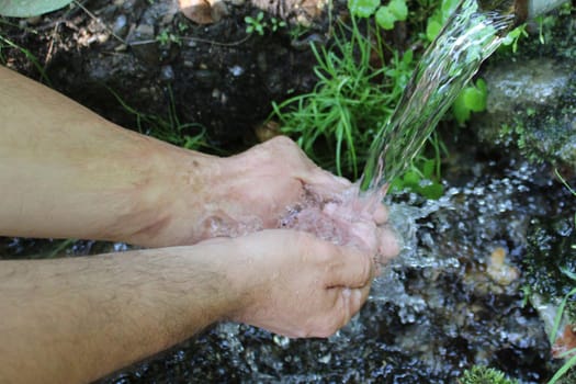 A man washes his hands at a spring in the forest. Blurred back natural background.