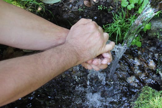 A man washes his hands at a spring in the forest. Blurred back natural background.
