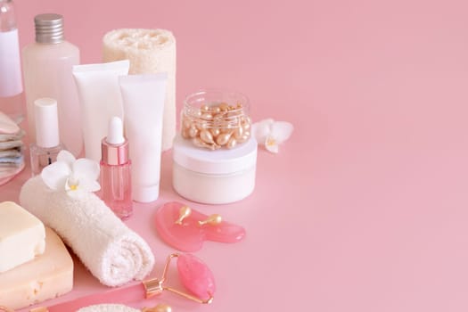 Natural cosmetic jars, skin care accesories and rose quartz face massagers with white orchid flower on light pink close up. Beauty products mockup. Everyday woman face care routine, Spa Treatments