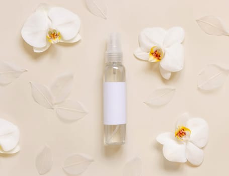 One pump dispenser bottle near white orchid flowers on light yellow top view, mockup. Skincare beauty product package. Exotic natural cosmetics, pastel minimal composition..