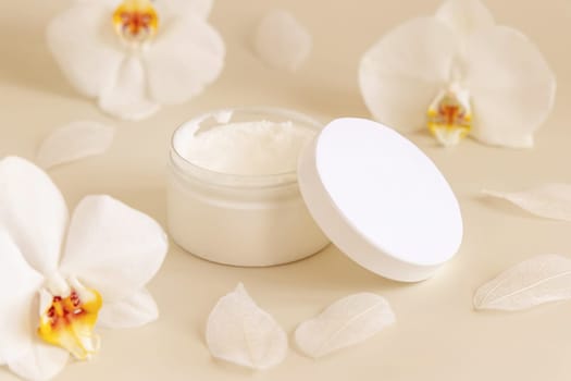 Opened Cream jar with a blank white lid near white orchid flowers on light yellow close up. Cosmetic packaging Mockup. Exotic natural cosmetics, romantic composition, everyday skincare routine..