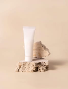White plastic cream tube on travertine stone on light yellow, close up, mockup. Skincare beauty product. Natural cosmetics. Minimal eco friendly composition..