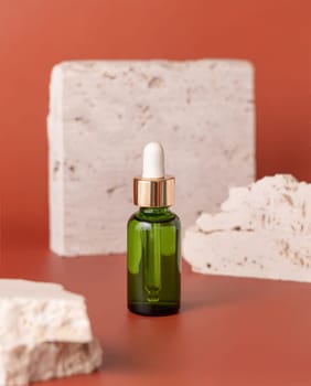 Green dropped bottle near travertine stones on pink close up, cosmetic mockup. Skincare beauty product. Natural cosmetics. Minimal composition..