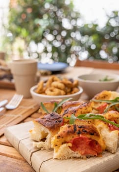 Italian summer appetizer focaccia with cherry tomatoes and rucola served outdoor with glasses of red wine. Tipical Apulian Dried bread, made in Salento. Local cousine. Vegetarian food
