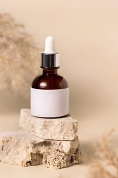 Brown dropper bottle with blank label on travertine stone near dry pampas grass on light yellow, close up, mockup. Skincare beauty product. Natural cosmetics. Boho composition..