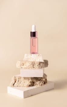 Pink glass cosmetic dropper bottle on beige travertine stones on light yellow close up, mockup. Skincare natural beauty product. Minimal eco friendly composition.